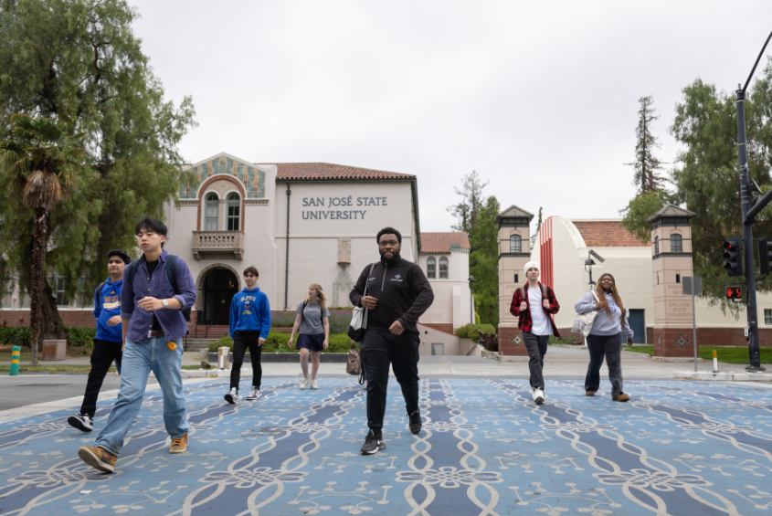 SJSU students crossing the street in a crosswalk at the edge of campus.