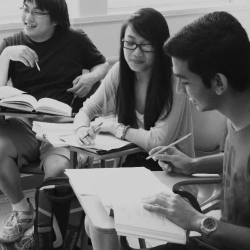 three students sitting at desks and having a discussion