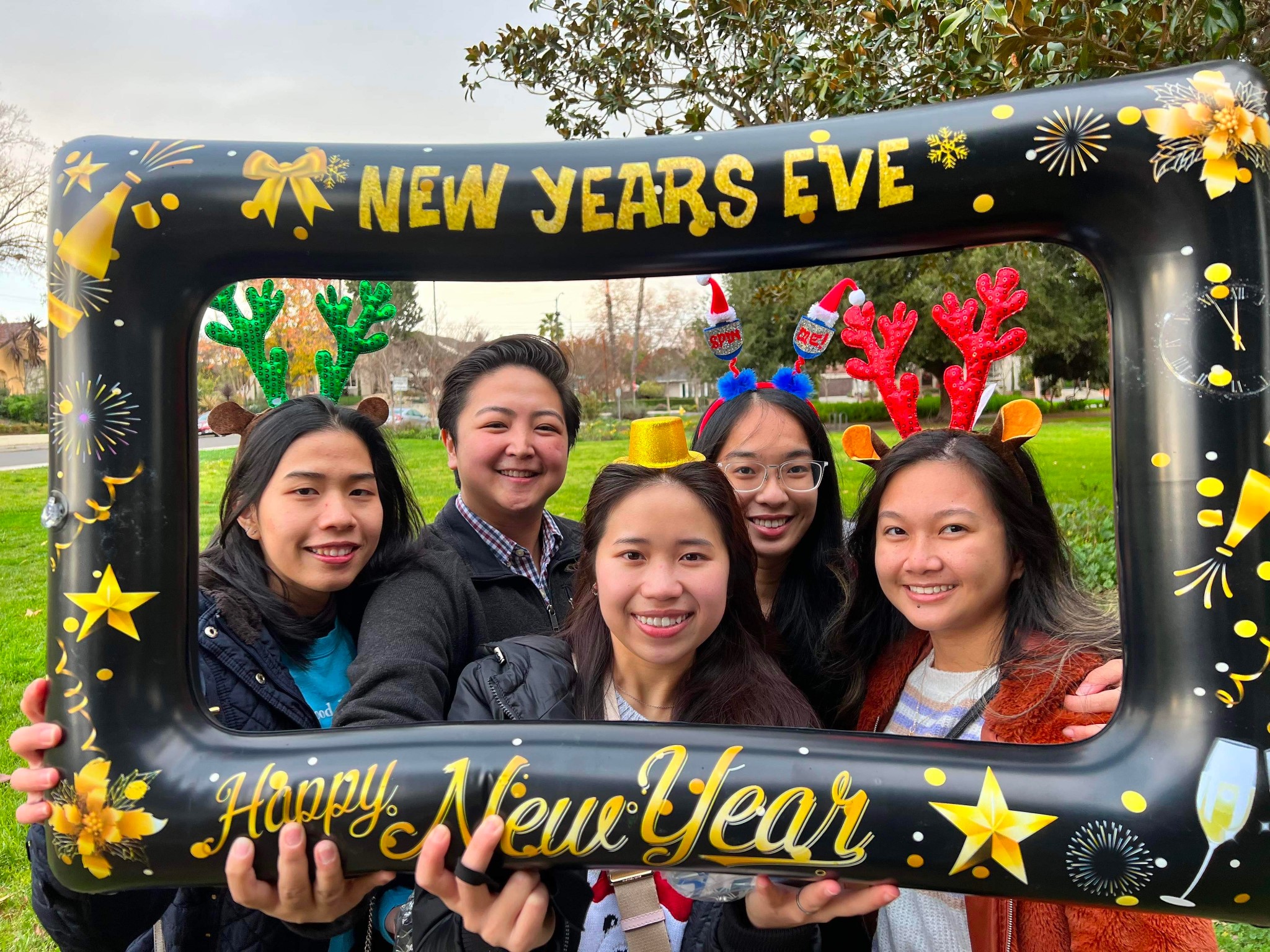 CNSA NYE Celebration Several CNSA members at a New Years Eve celebration, stading in a grass park, posing with an inflatable picture frame, smiling at the camera.