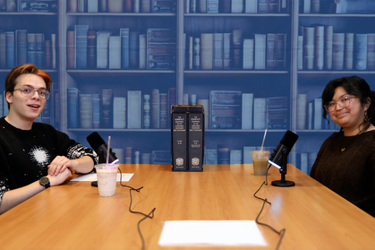 Two team members seated opposite each other at a table with bookshelf backdrop